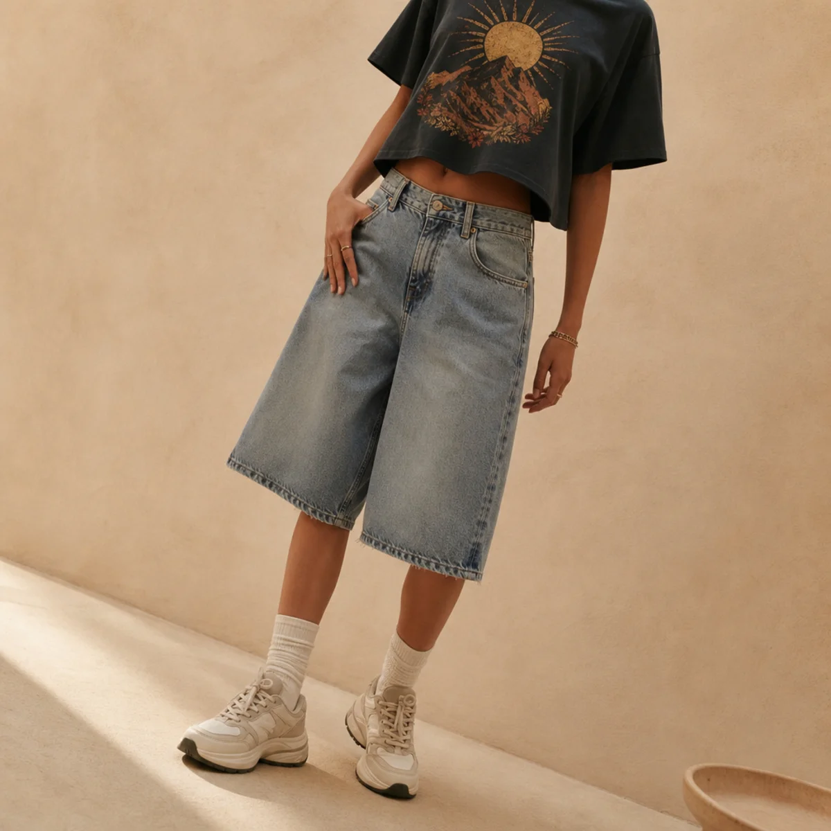 Faceless waist-down shot of baggy denim jorts with a cropped graphic tee and chunky sneakers