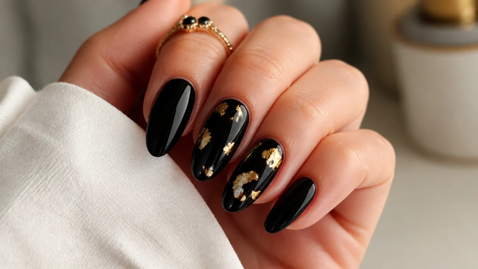 Black almond nails with thin gold foil leaf accents scattered across two nails
