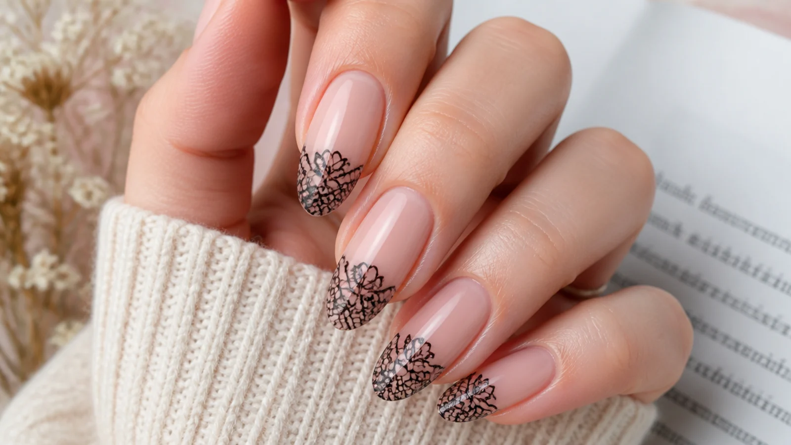 Sheer nude almond nails with fine black lace patterns painted over the tip half