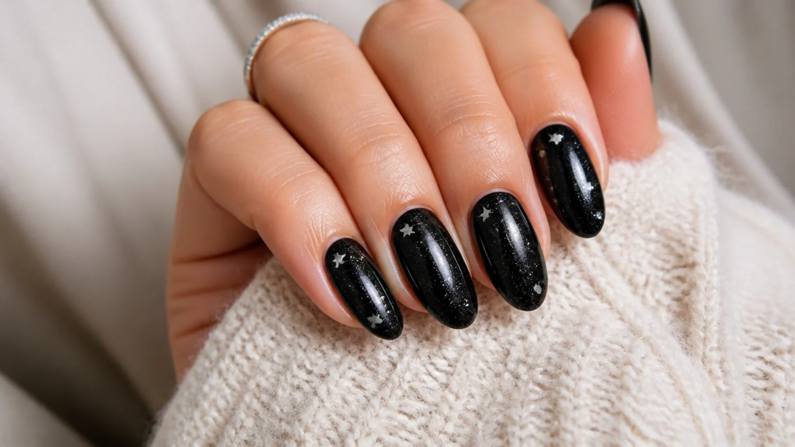 Deep black almond nails with tiny silver stars and fine shimmer scattered across the surface