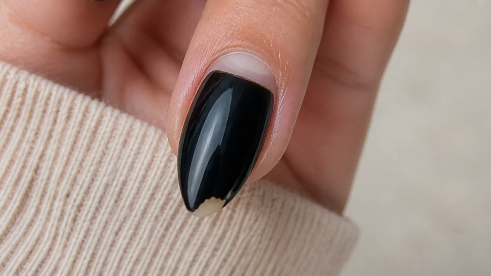 Close-up of a black almond nail showing a chipped free edge and a regrowth gap at the cuticle