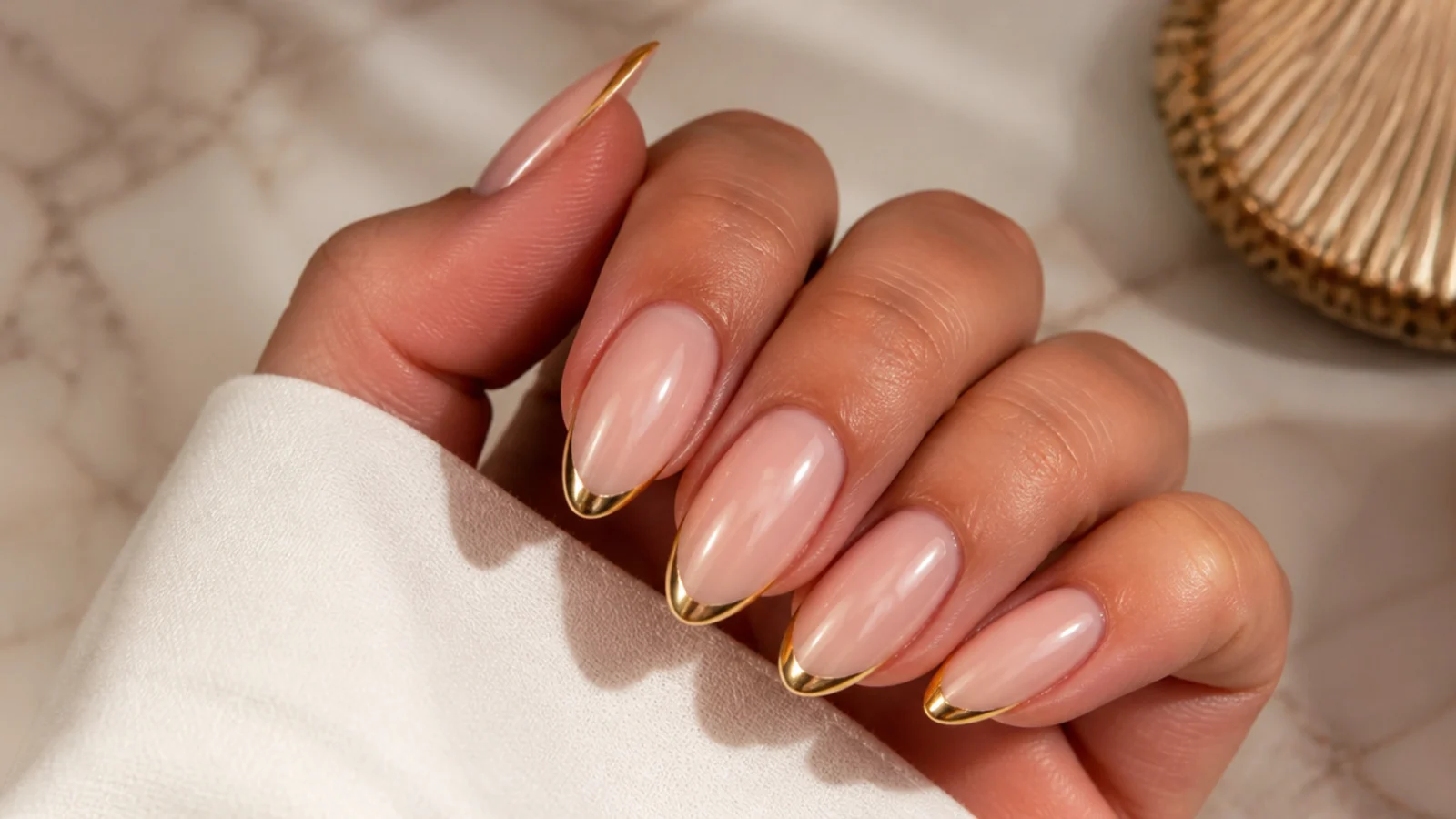 Long almond nails with a thin gold chrome French tip over a sheer nude base