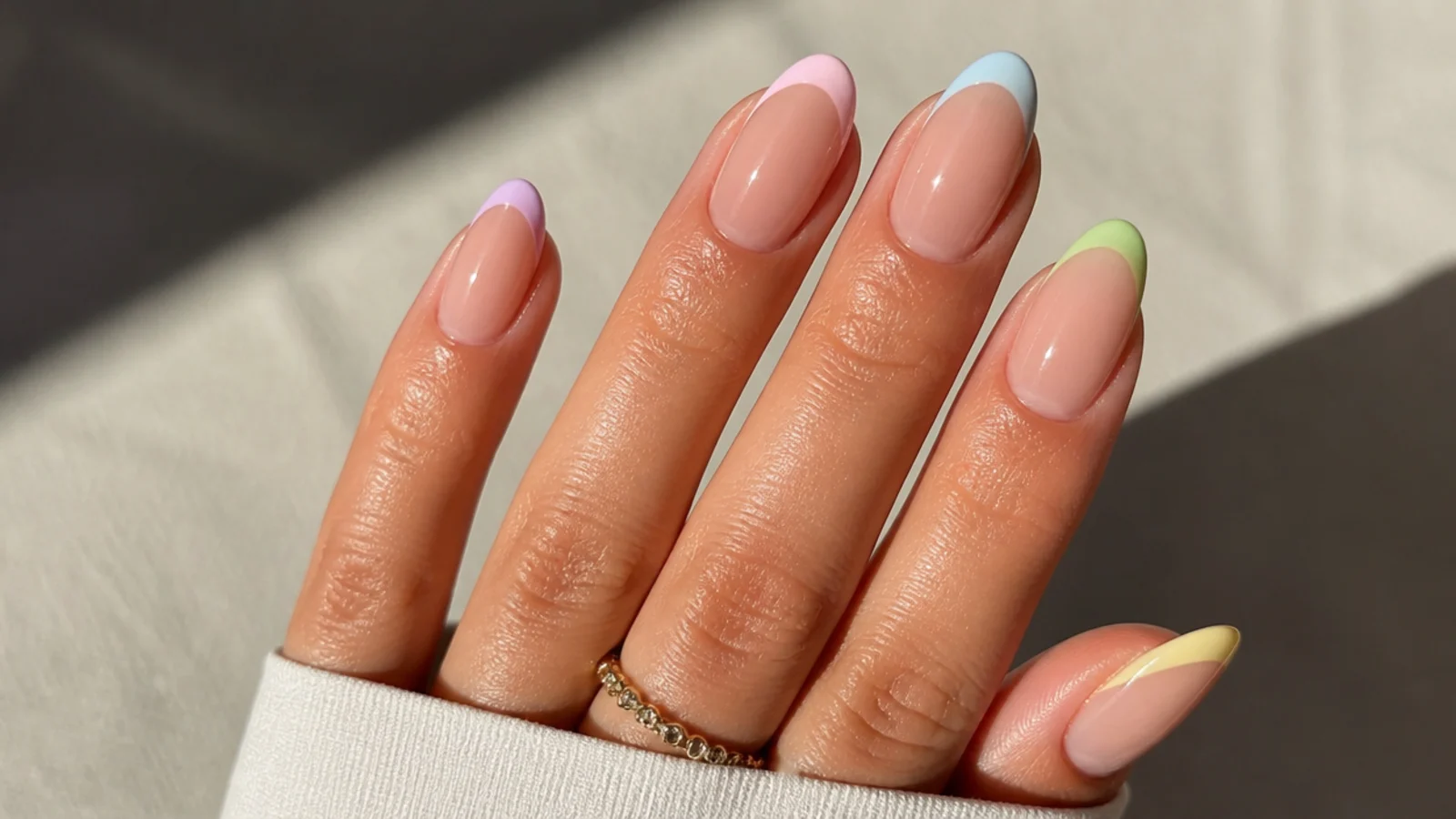 Oval french tip nails with five different pastel tip colors across one hand on a nude base