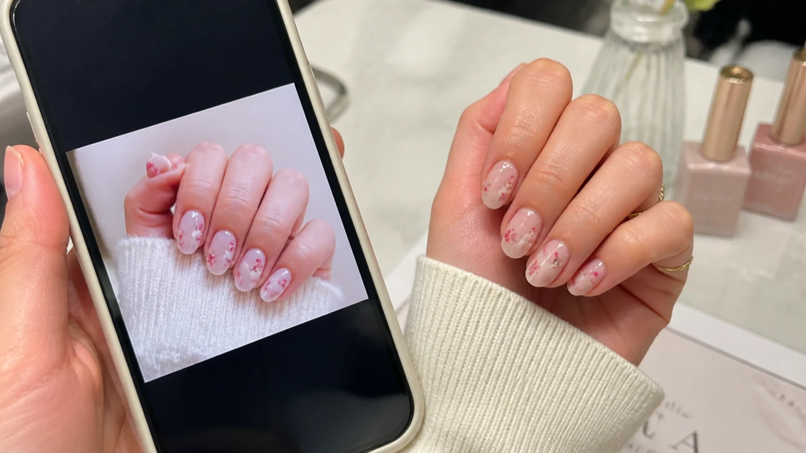 Phone showing short almond nail reference photos held beside a hand at a nail salon table