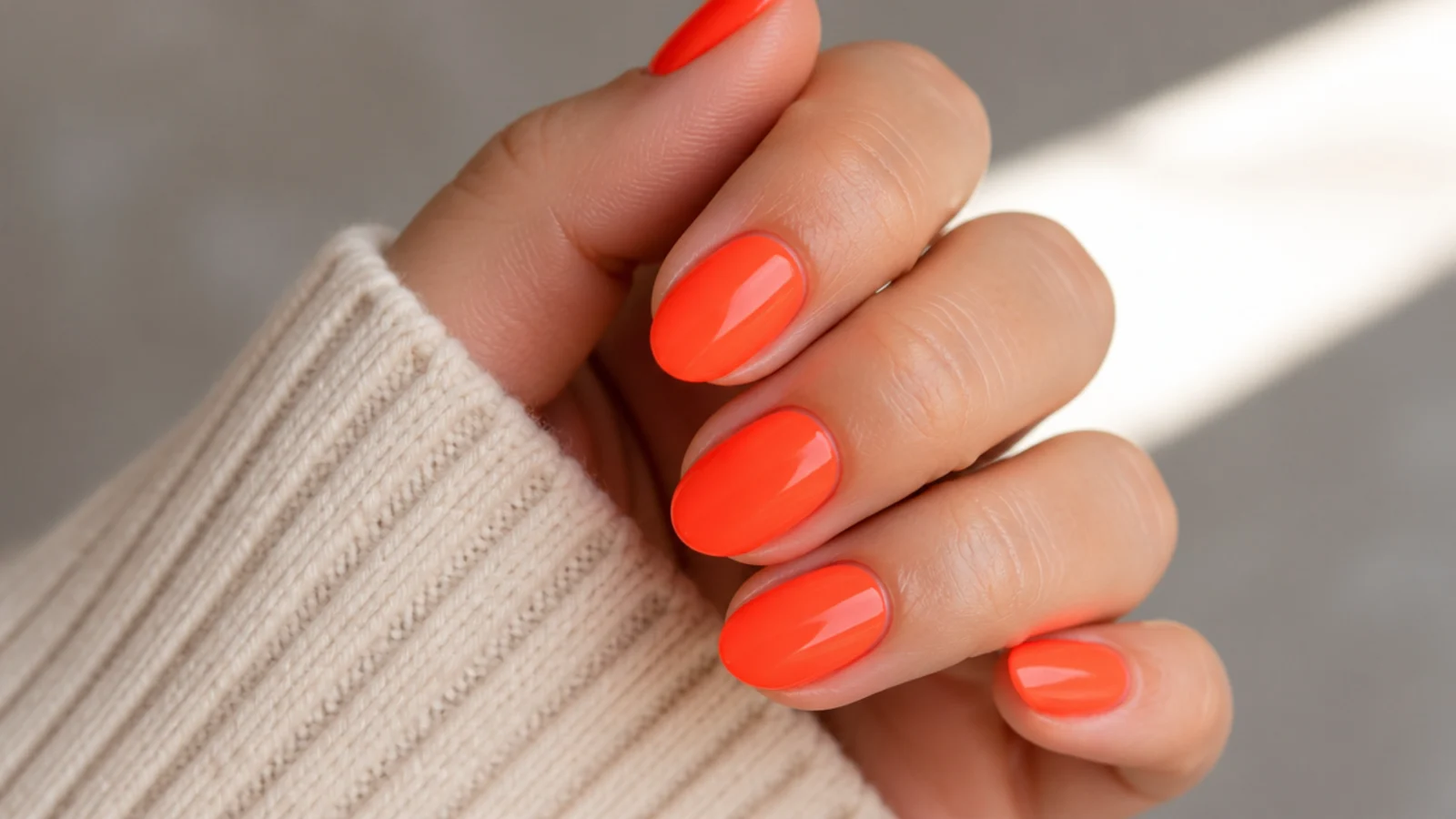 Short almond nails in neon coral orange with a bright opaque finish