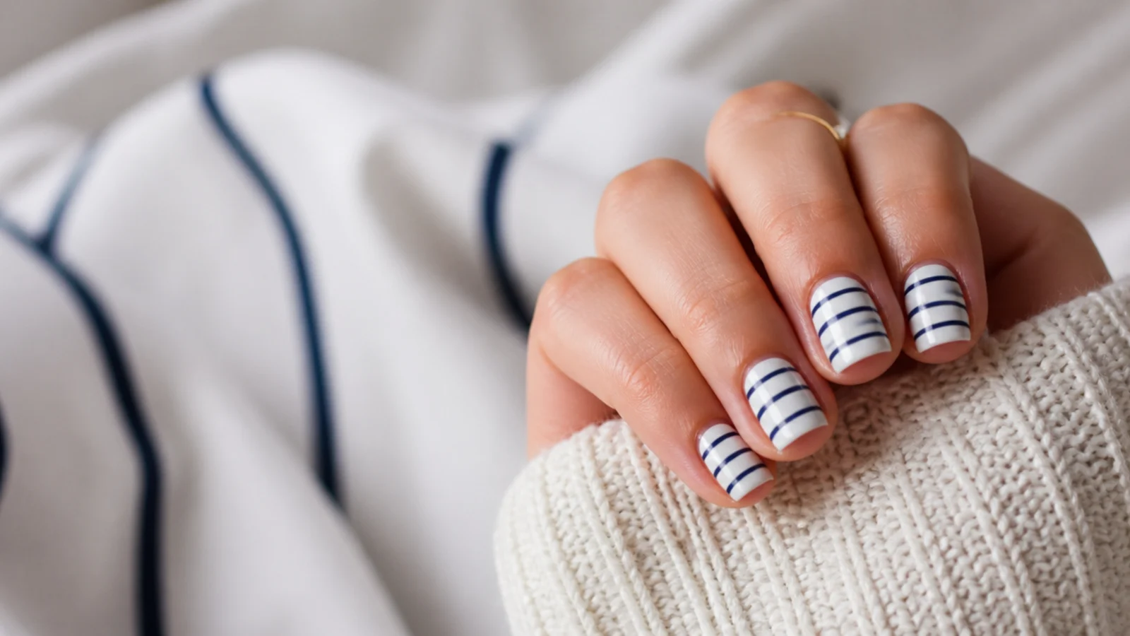 Short square nails with thin navy horizontal stripes over a white base in a nautical pattern