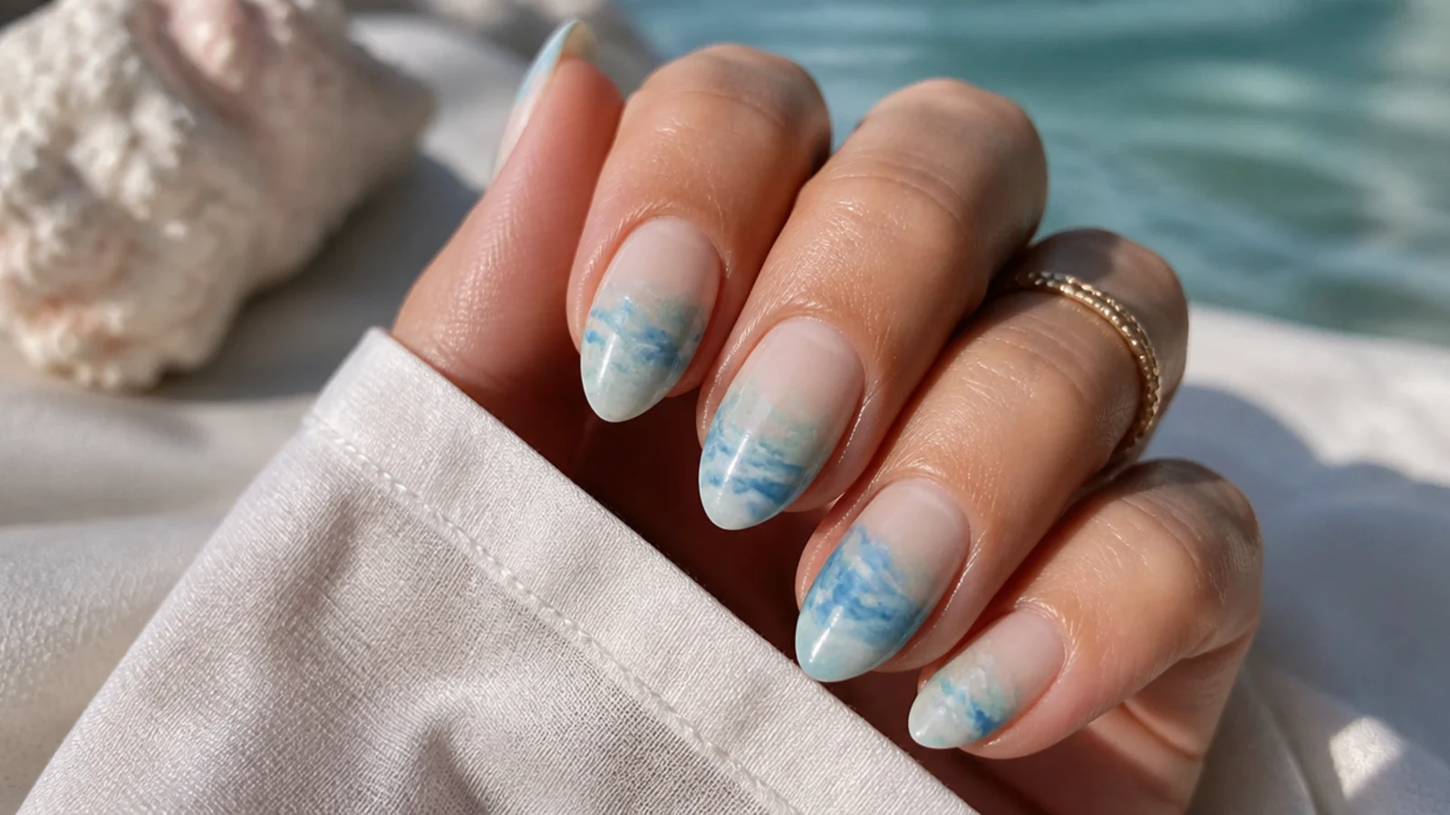 Almond nails with a soft watercolor ocean wash in light blue and aqua bleeding across a sheer base