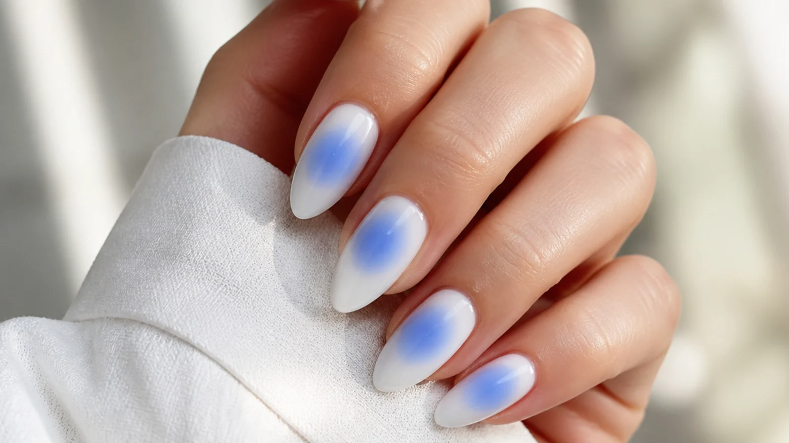 Almond nails with a blue aura halo airbrushed into the center of each pale nail like glowing water