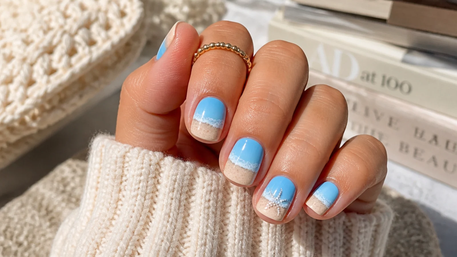 Short squoval nails with a sponged blue-to-sand ocean gradient, a white wave foam line and one dotted shell accent