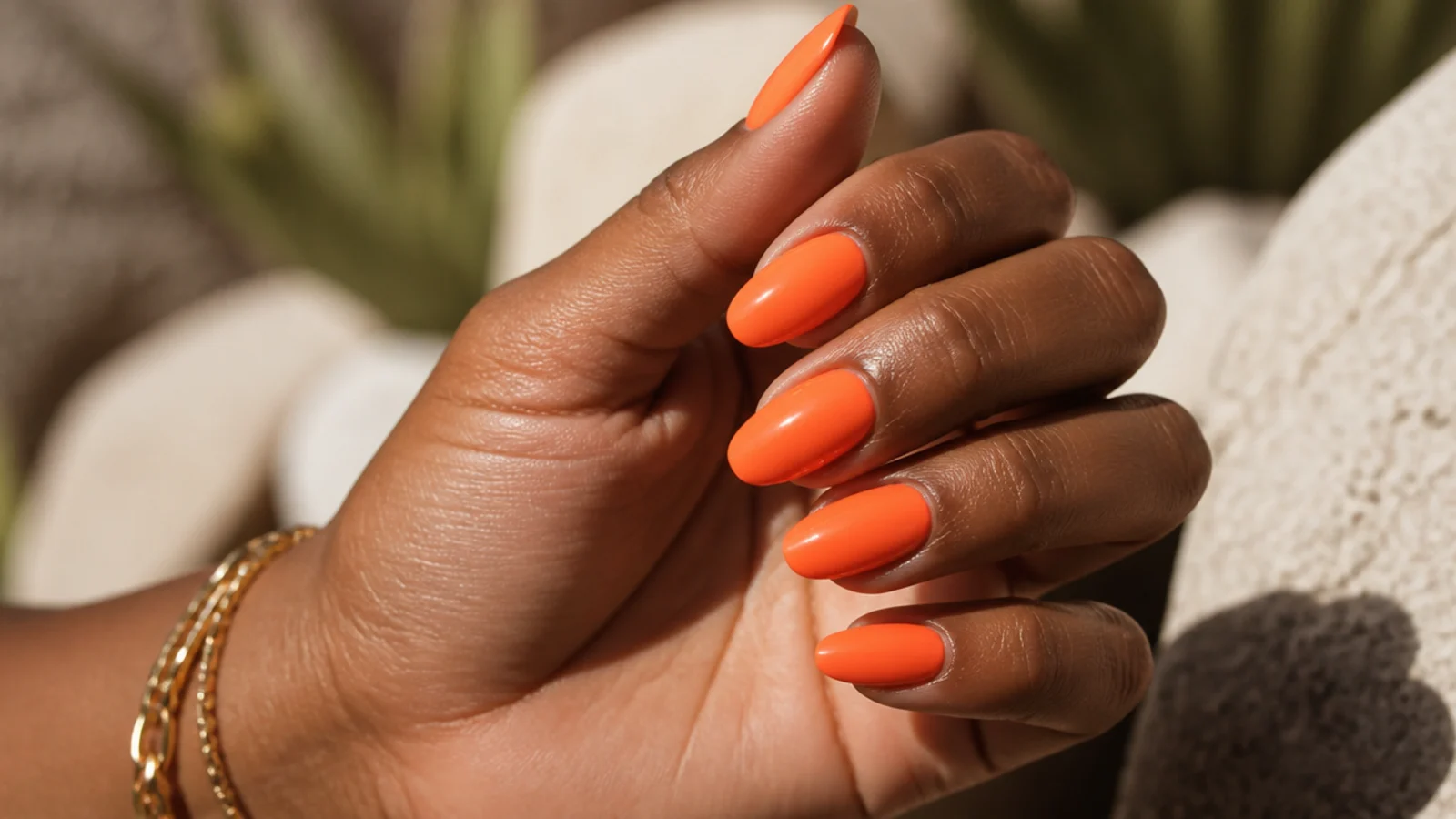 Neon orange nails glowing against a deep tan on a hand in bright daylight