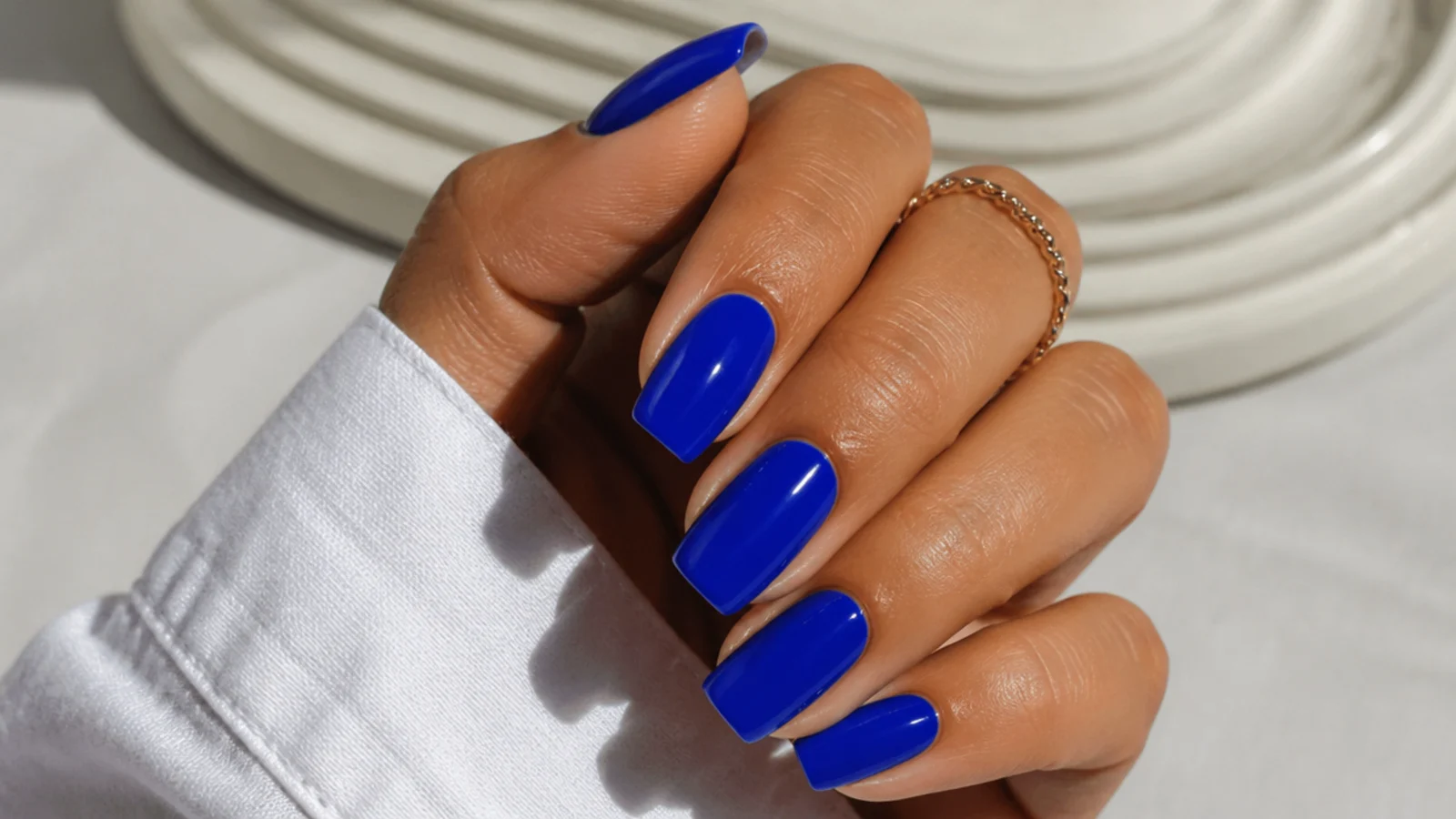 Vivid cobalt blue nails on a tanned hand with a saturated glossy finish