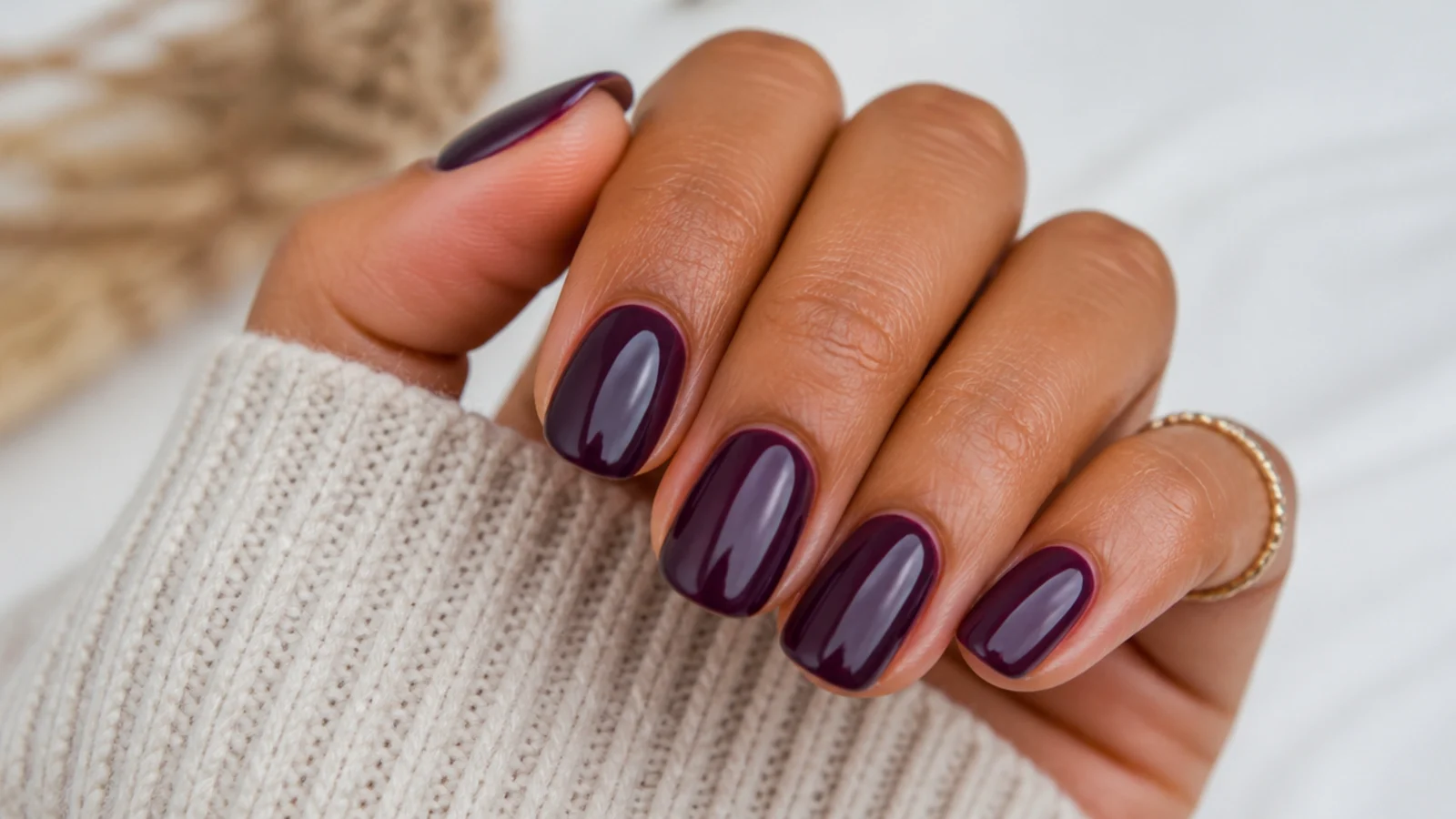 Deep plum purple nails on a tanned hand with a glossy jewel finish