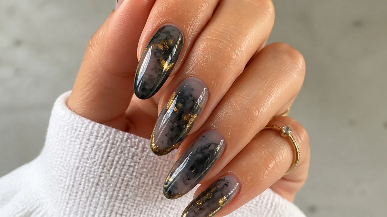 Black blooming gel nails with gold foil accents over inky diffusion
