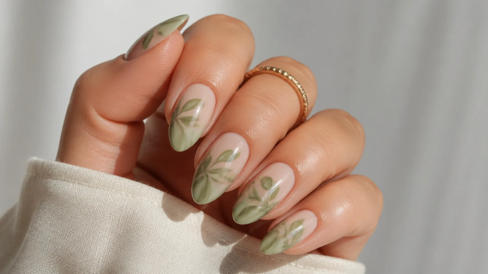 Soft sage-green leaf shapes diffused over a nude base on almond nails