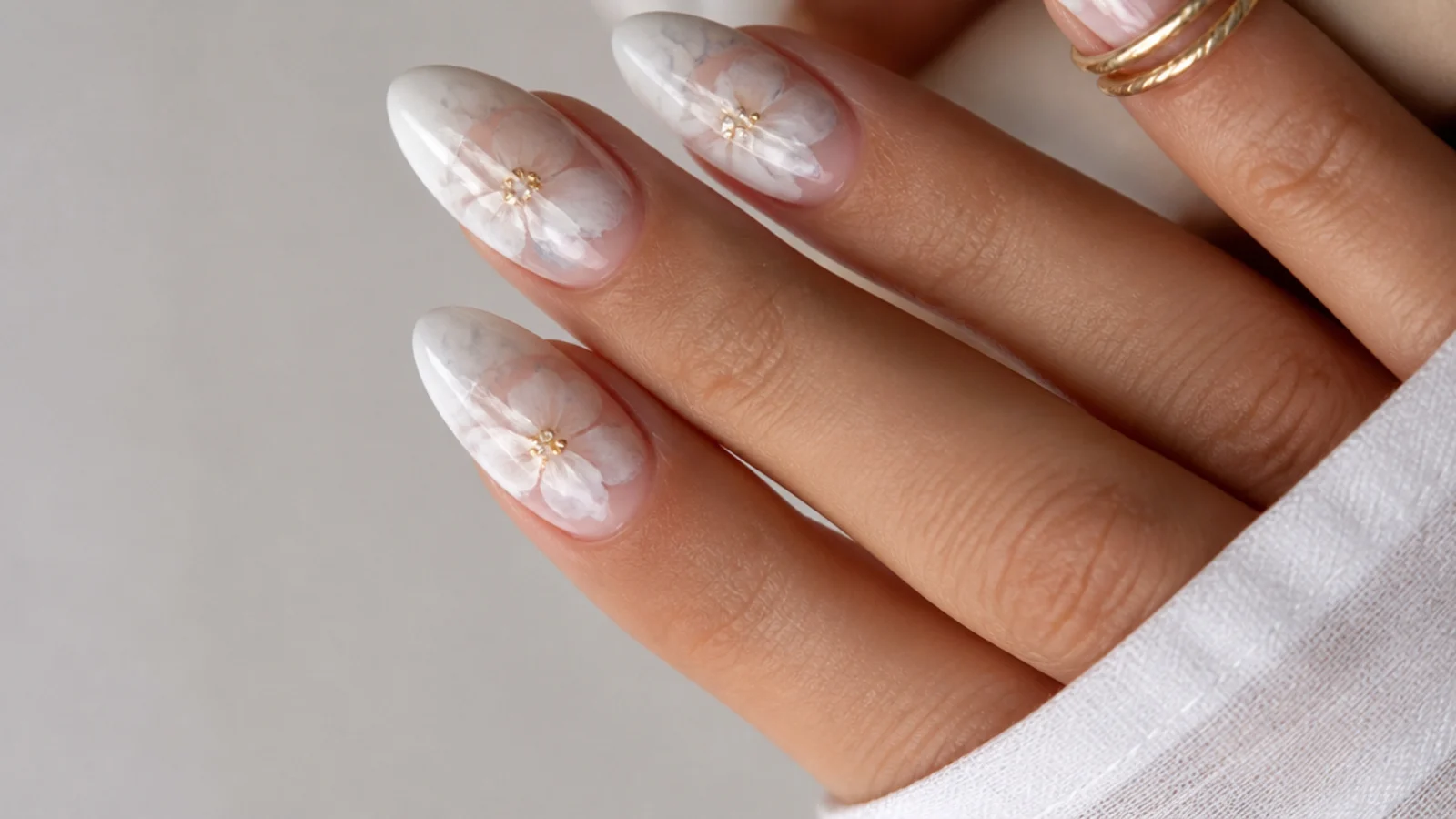 Soft white watercolor blooming gel nails in an almond shape on a plain background