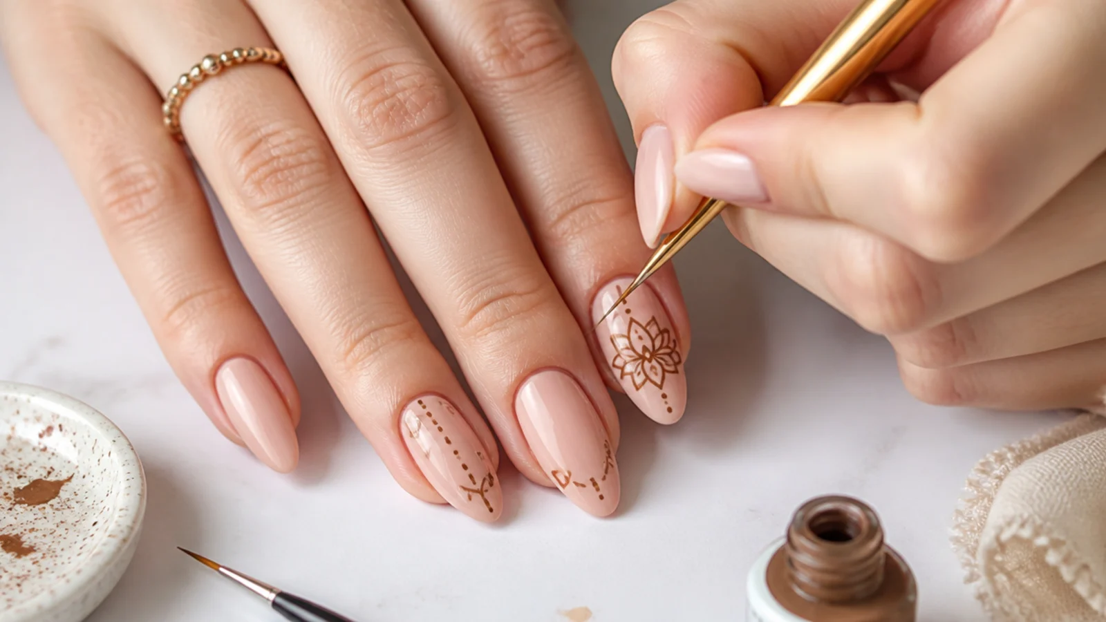 At-home boho nail supplies with a liner brush painting a fine mandala on a nude nail