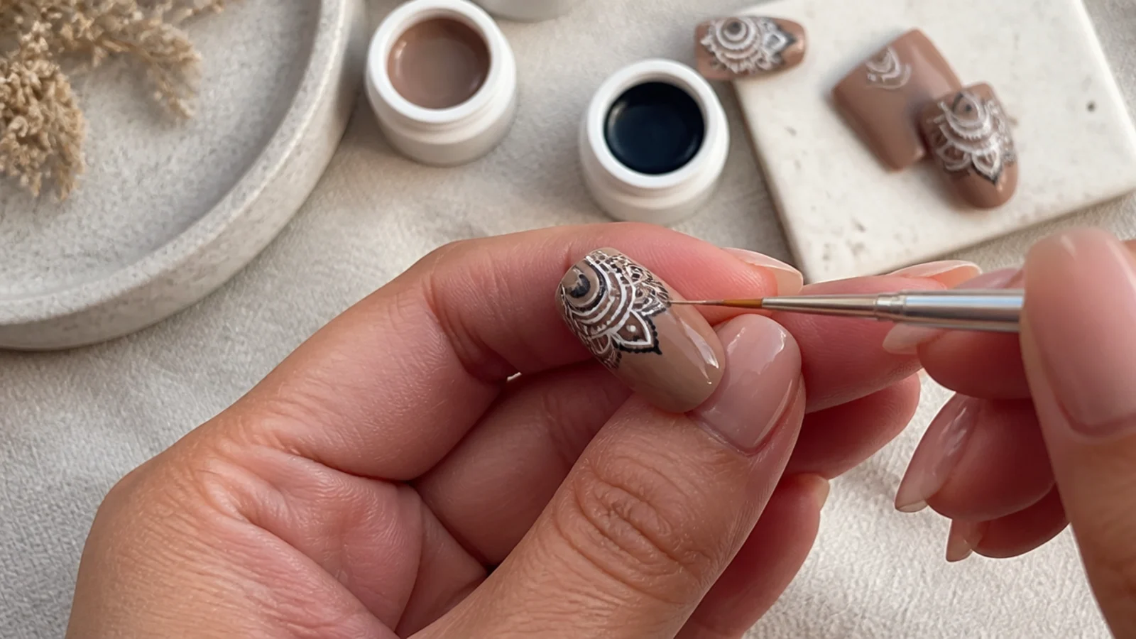 Boho nail supplies with a liner brush drawing a mandala on an earth-tone nail