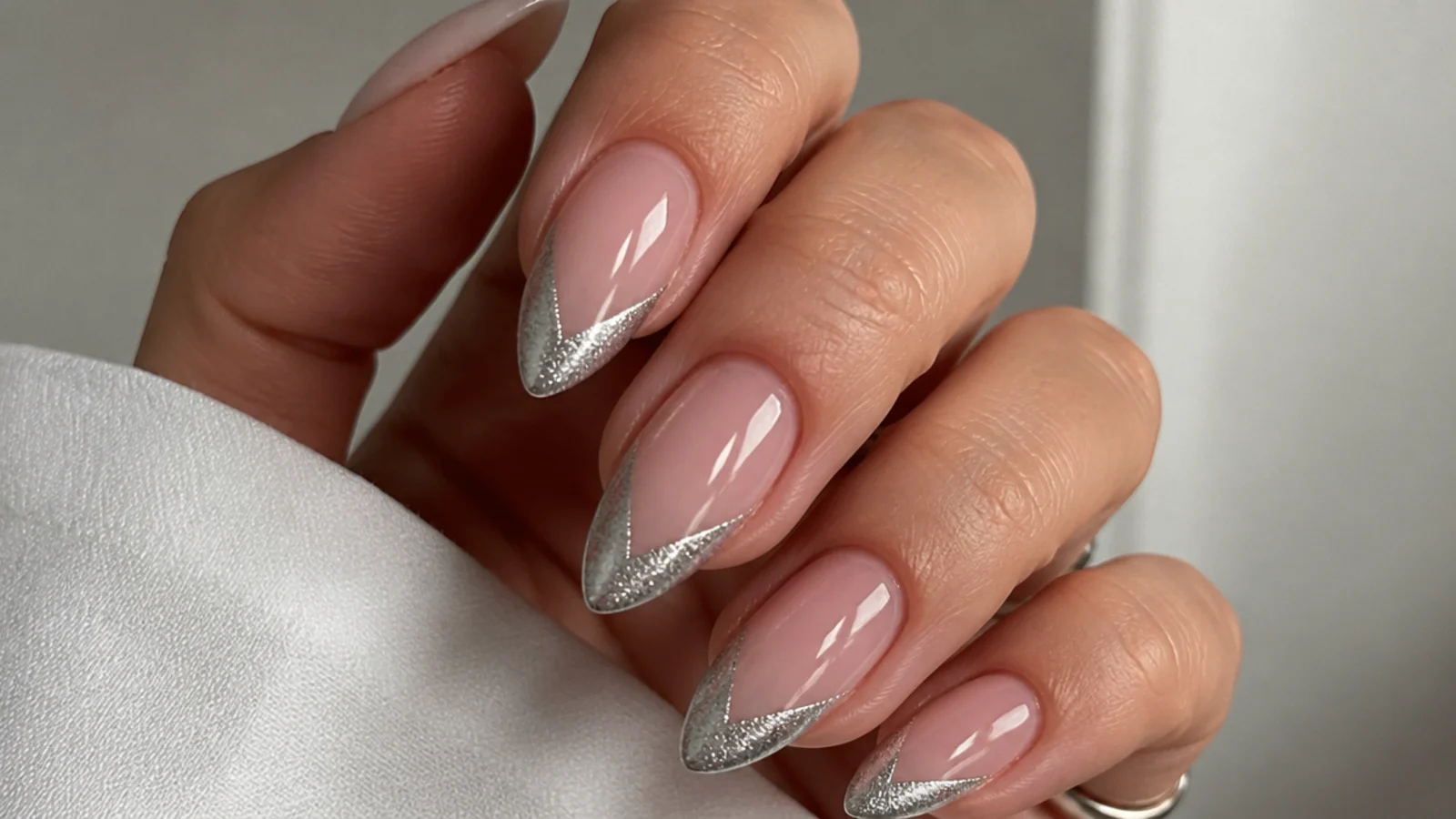 Almond nails with a nude base and a silver magnetic cat eye french tip shaped as a deep V