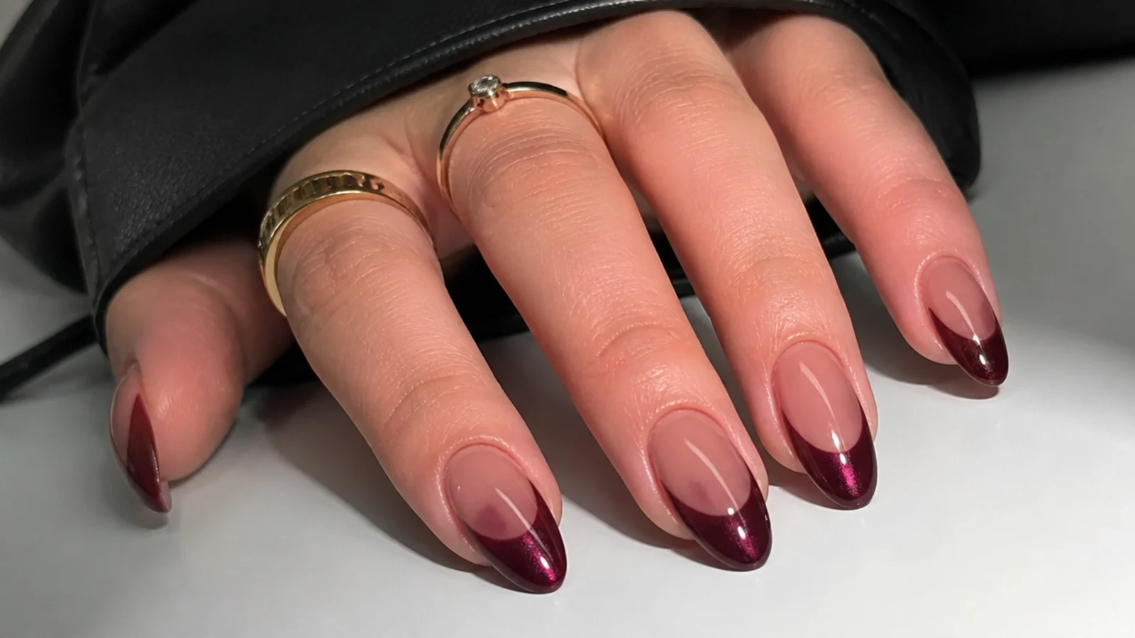 Deep oxblood cat eye french tip nails on almond shape with a moody light stripe