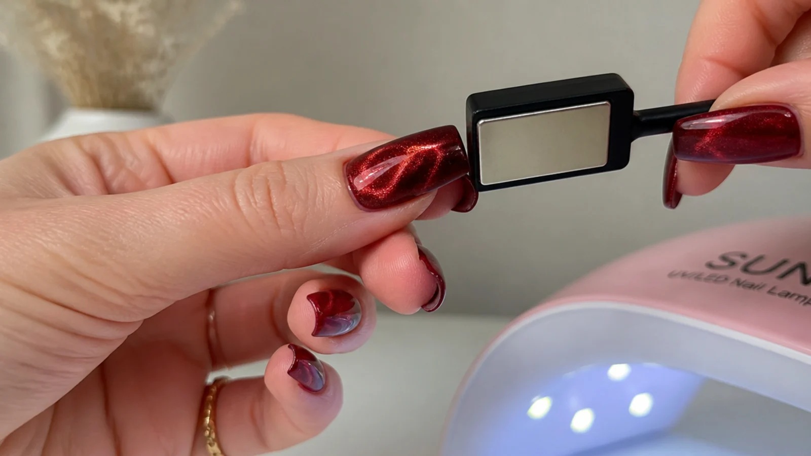 Red magnetic gel, a magnet and a lamp beside a nail mid-magnetizing at home