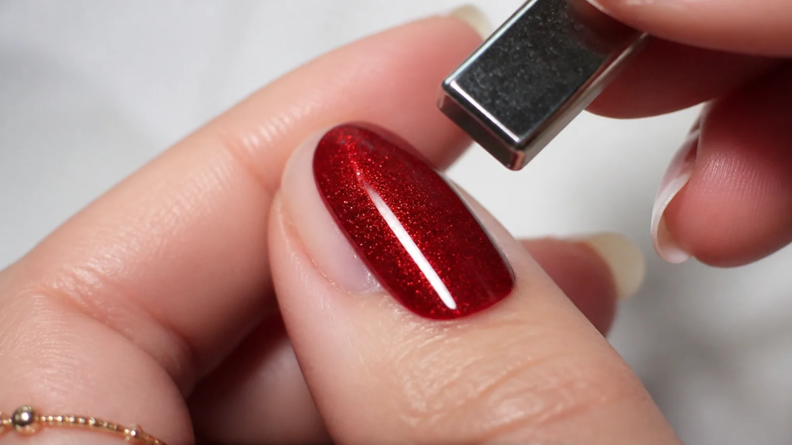 A magnet held just above a wet red gel tip pulling a bright light stripe on a nail