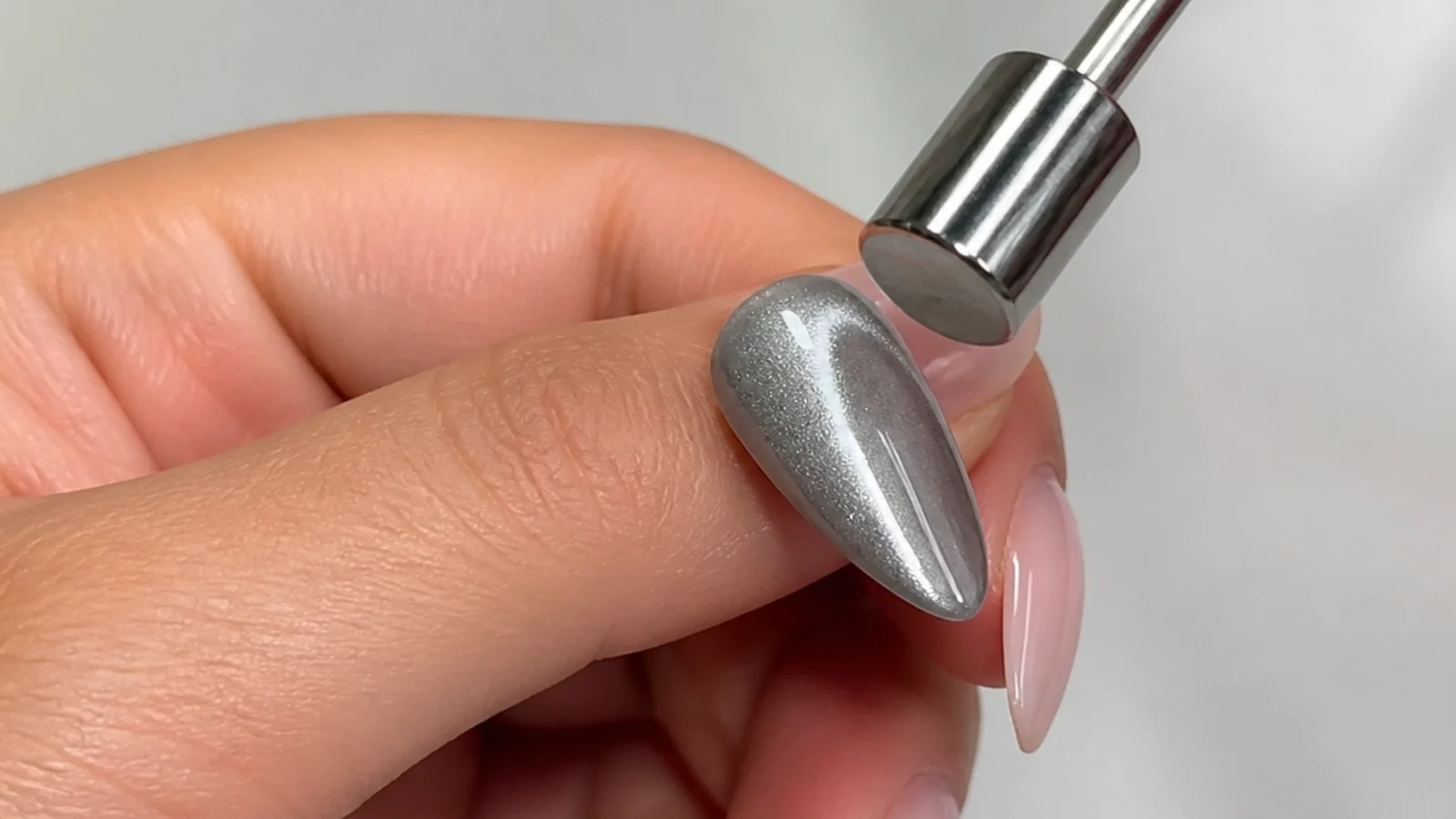 A magnet hovering above a wet silver gel tip pulling iron particles into a light stripe