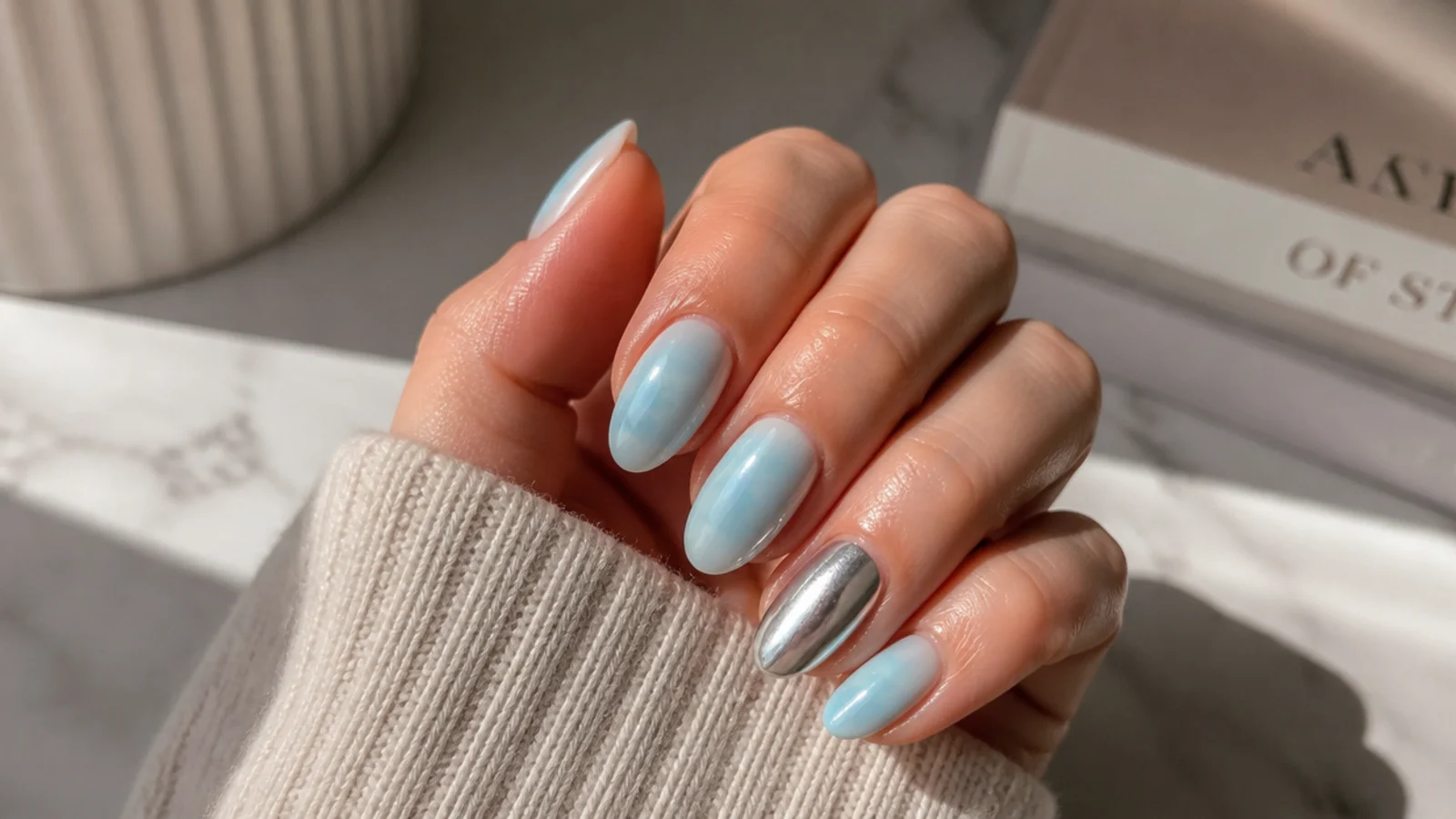 Hand with four soft blue aura nails and one silver chrome accent nail on the ring finger
