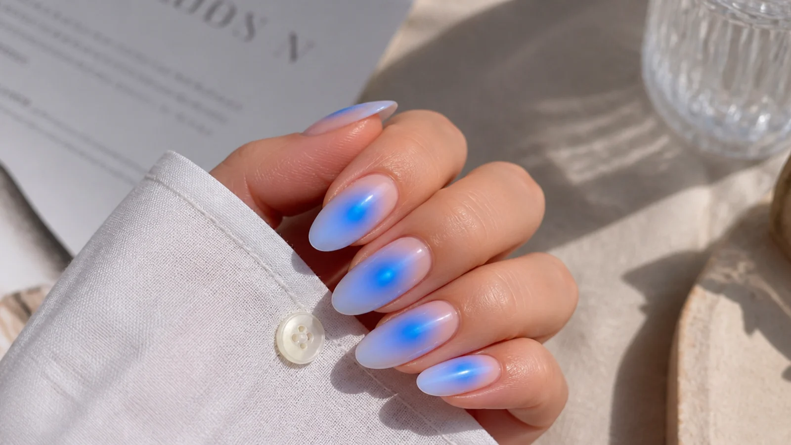 Blue aura almond nails with an oval halo following the tapered curve of the nail