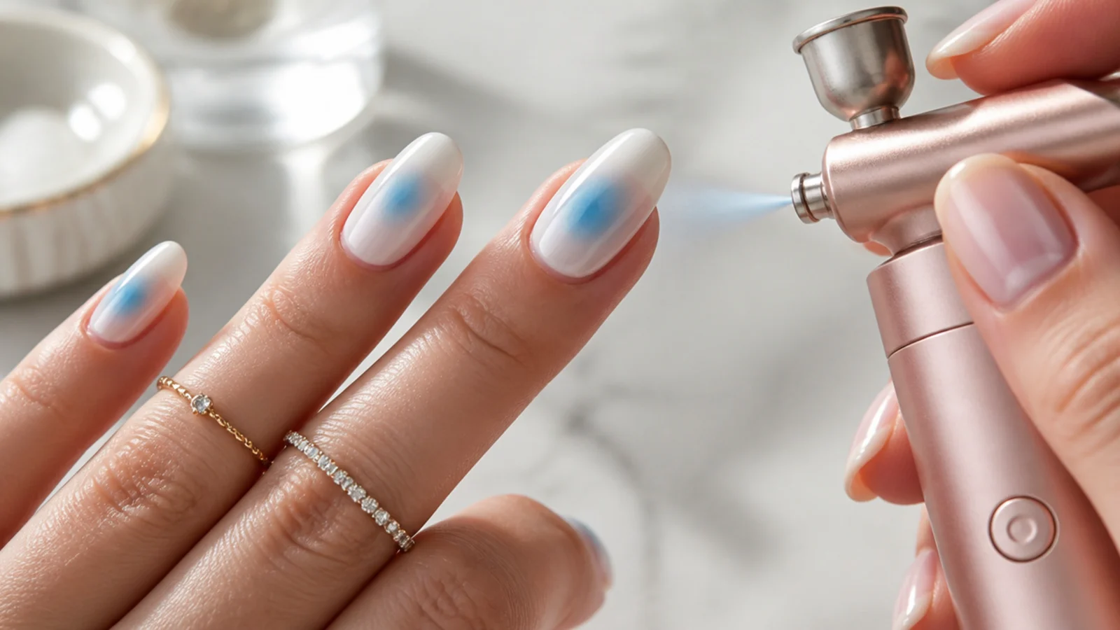 A cordless mini nail airbrush spraying a soft blue aura halo onto an almond nail