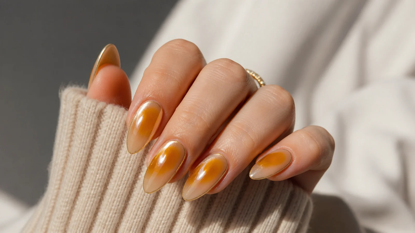 Almond nails with a warm amber aura halo under a gold chrome layer on a beige base