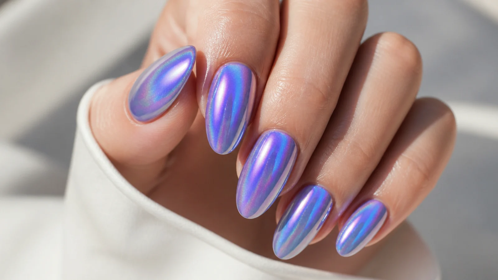 Long almond nails with a blue and violet aura halo under a holographic chrome finish splitting light