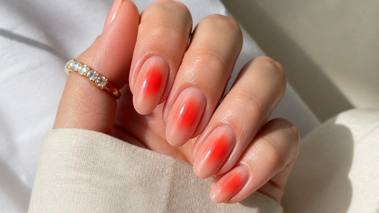 Coral red aura nails with an orange-leaning red glow on a peachy nude base