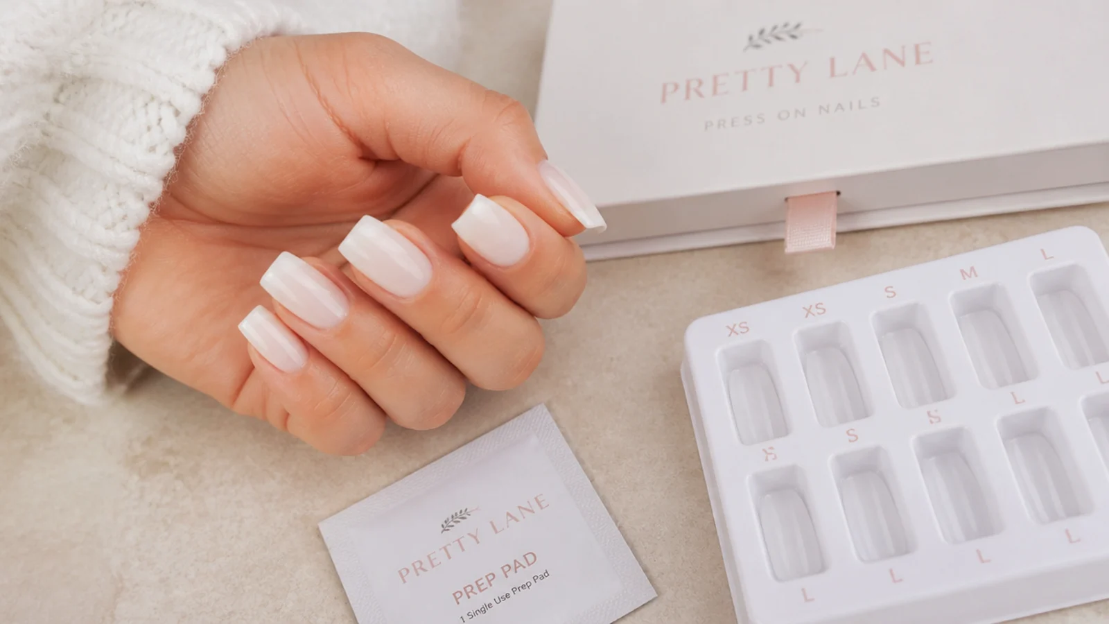 Short coffin press-on nails in a soft milky shade laid out beside a sizing tray and prep pad