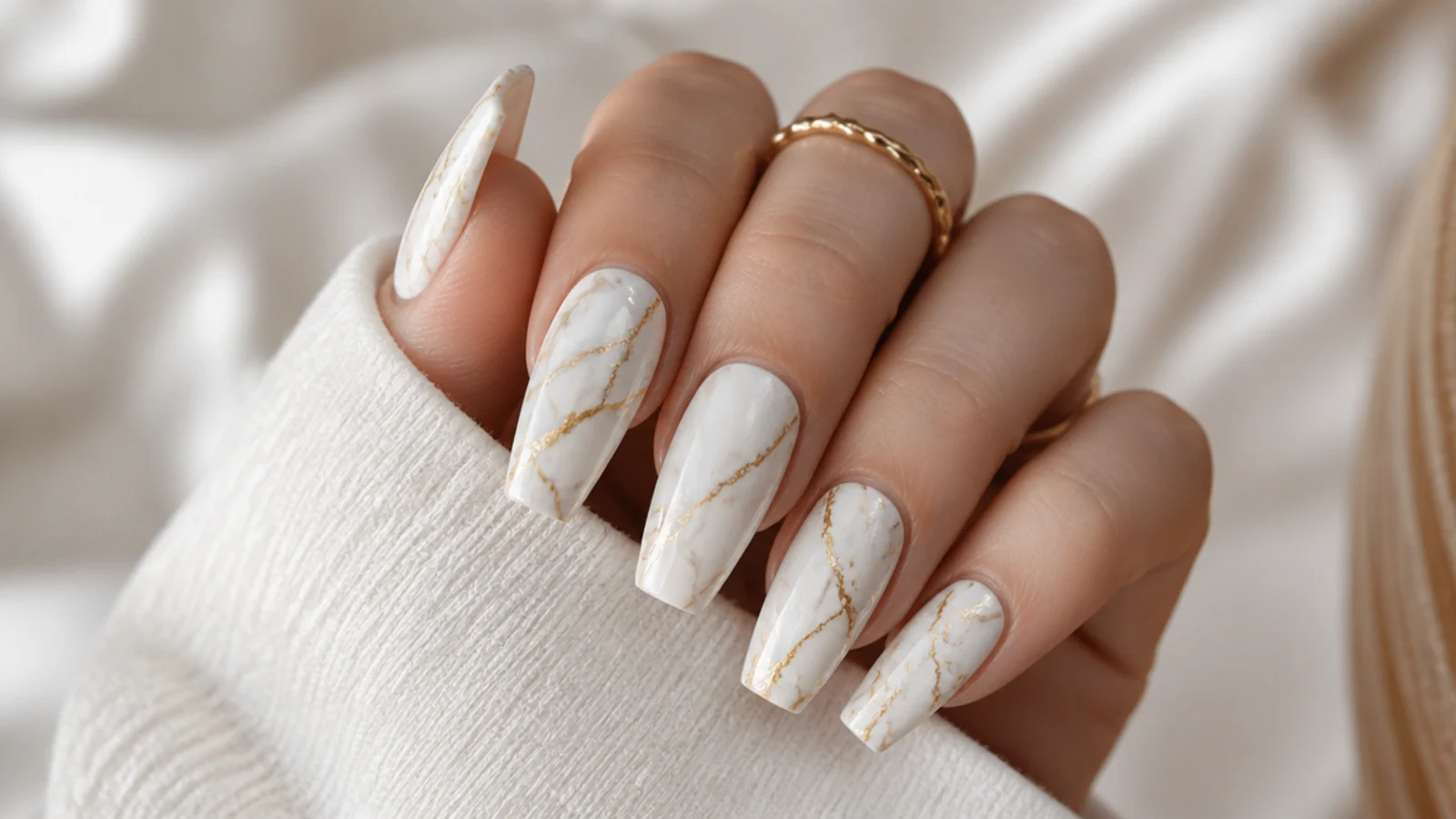 Long coffin nails with white marble veining and fine gold lines on a cream base
