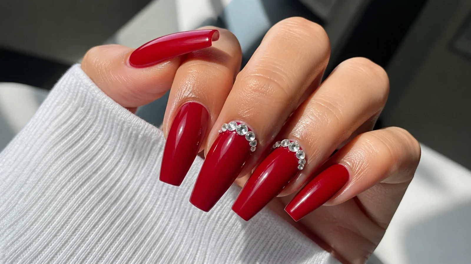 Red coffin nails with clear rhinestones clustered near the cuticle on two nails