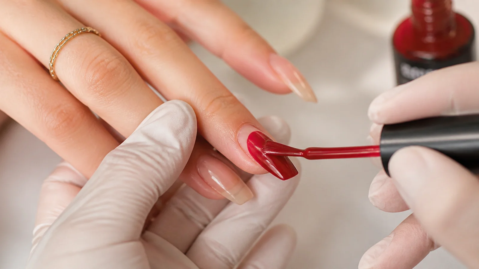 Thin coats of red gel being applied to a coffin-shaped nail with a flat tip