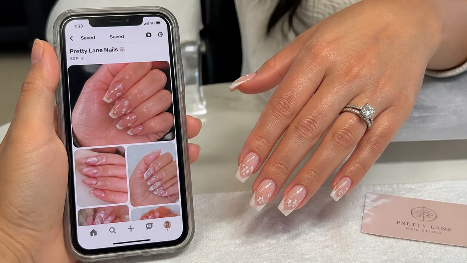 Phone showing saved acrylic nail reference photos held beside a hand at a salon table