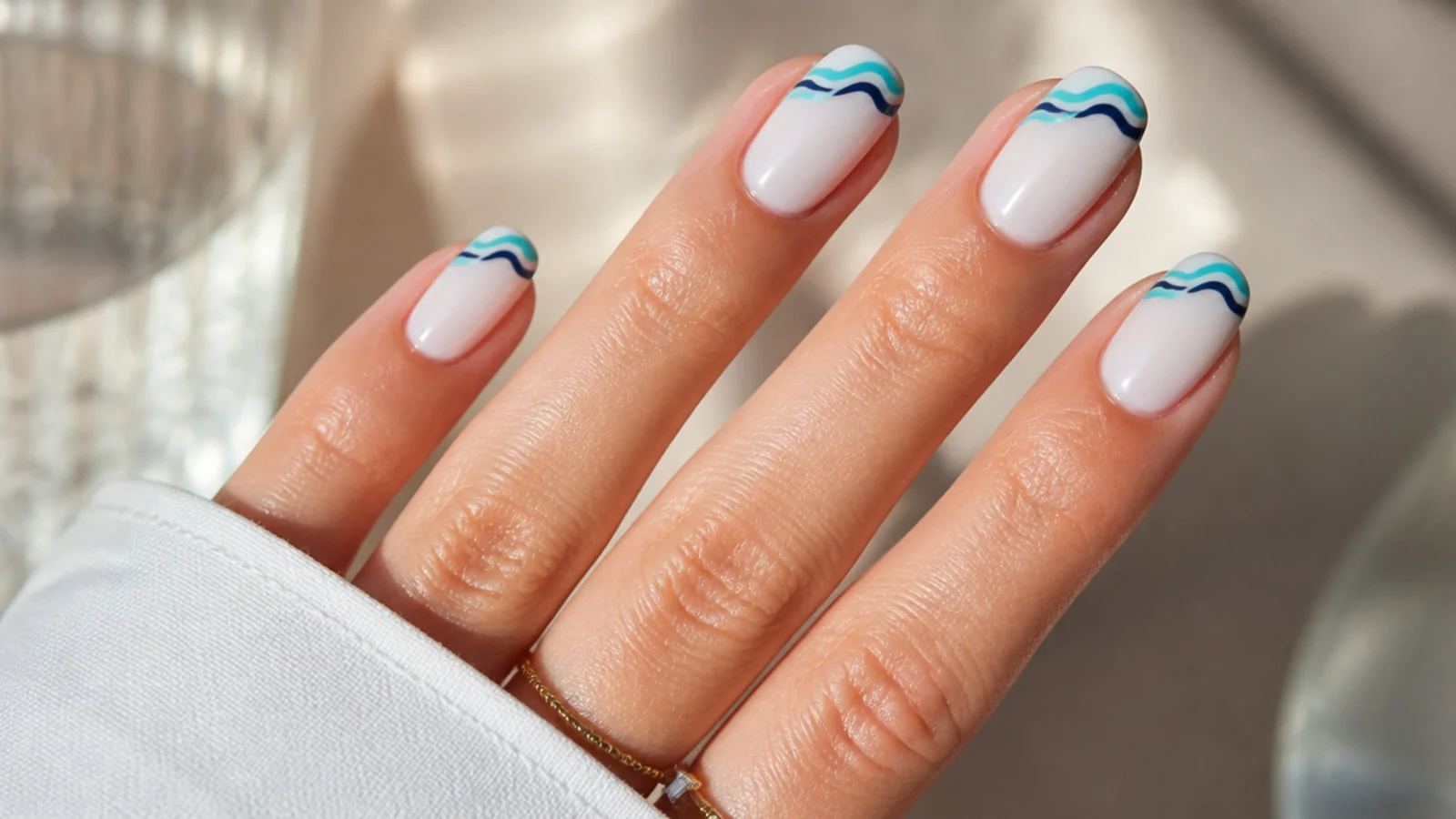 Milky white nails with hand painted turquoise and navy wavy lines across the tips