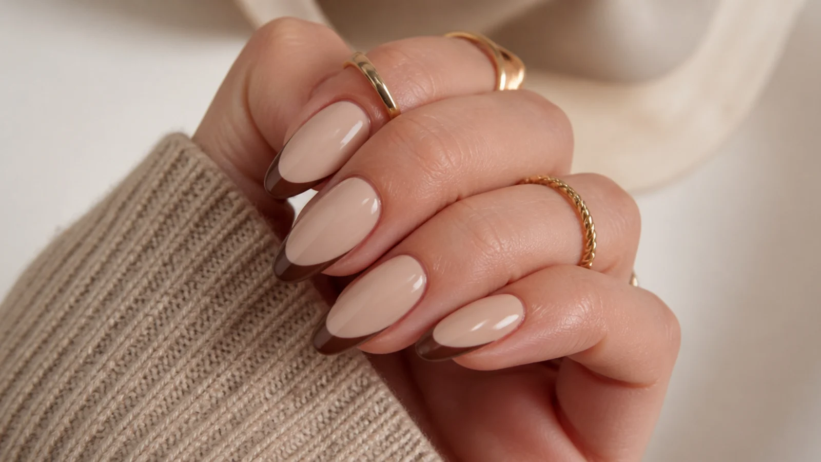Medium almond nails with mocha brown French tips over a warm beige base