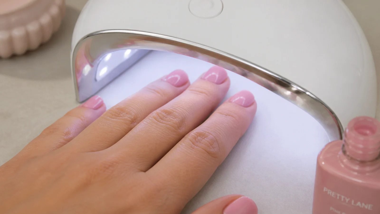 Hand under a small LED nail lamp curing a coat of pink gel polish on short nails