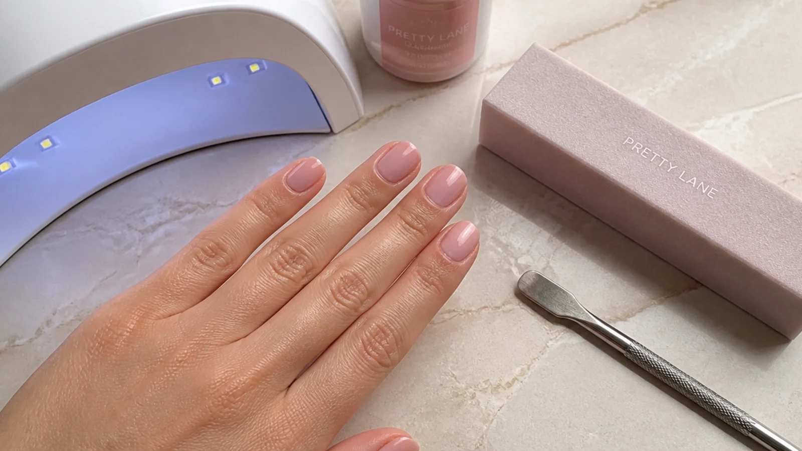 Beginner nail setup with sheer pink gel, a buffer, cuticle pusher and a small UV lamp