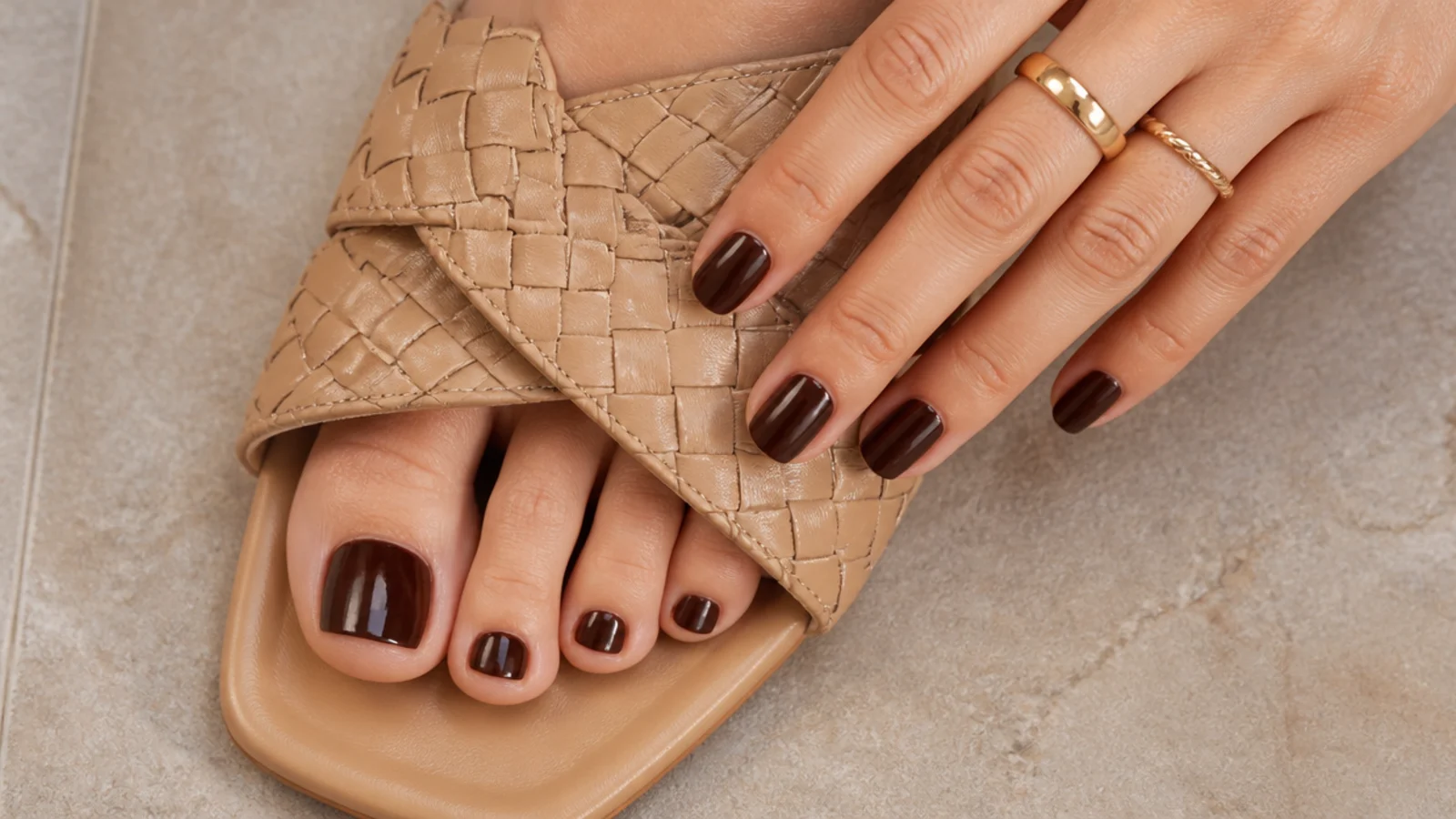 Deep chocolate brown toe nails with a glossy finish in woven flat sandals