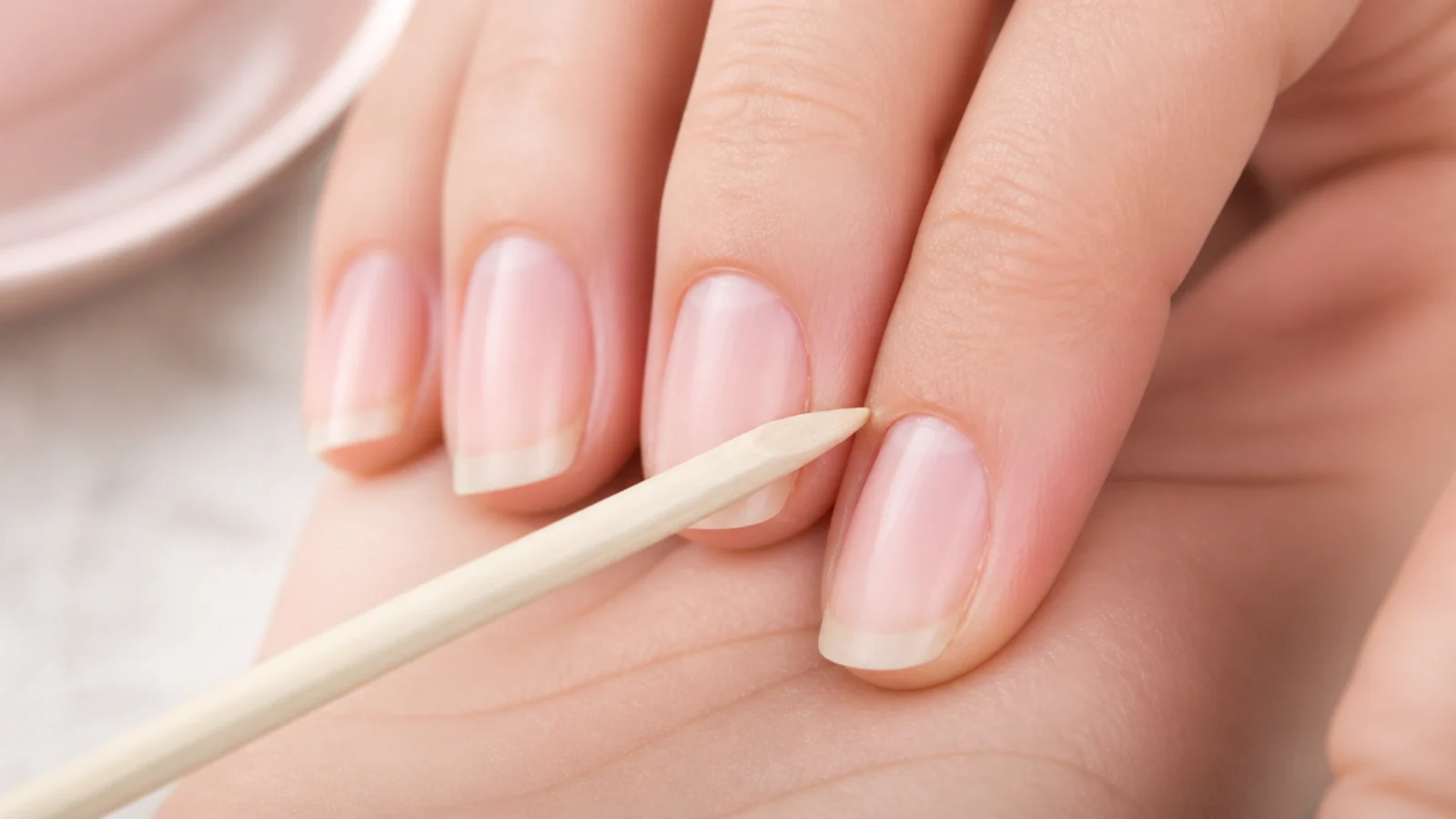 A wood cuticle pusher gently pushing back the eponychium on a bare nail before polish