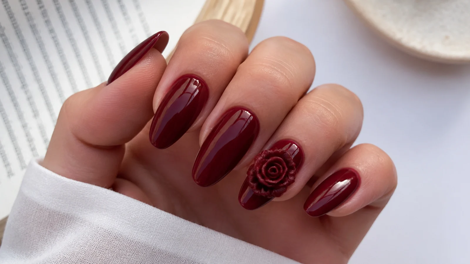 Wine red almond acrylic nails with a sculpted 3D rose accent