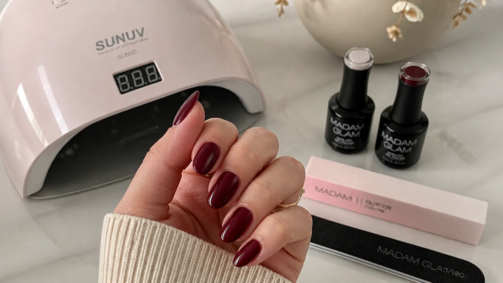 Deep berry gel, lamp and buffer laid out for a dark feminine set at home