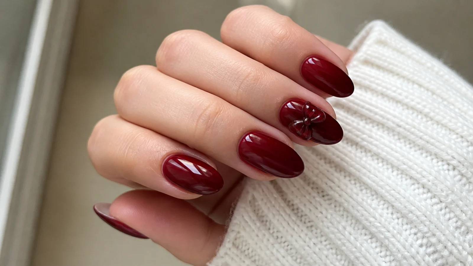 Deep cherry red dark feminine nails with a small 3D bow accent