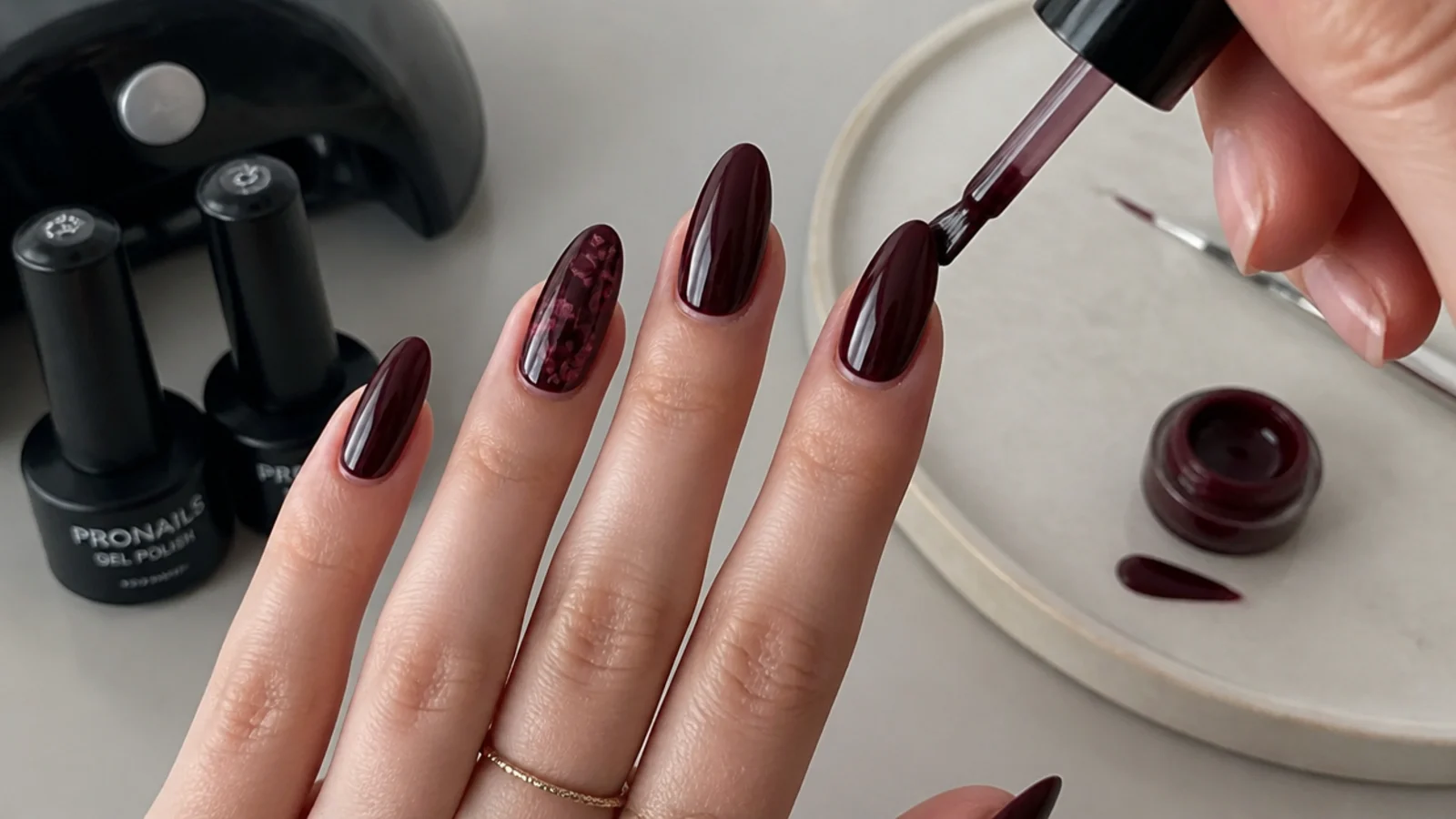 At-home dark feminine gel supplies and a deep berry nail mid-application