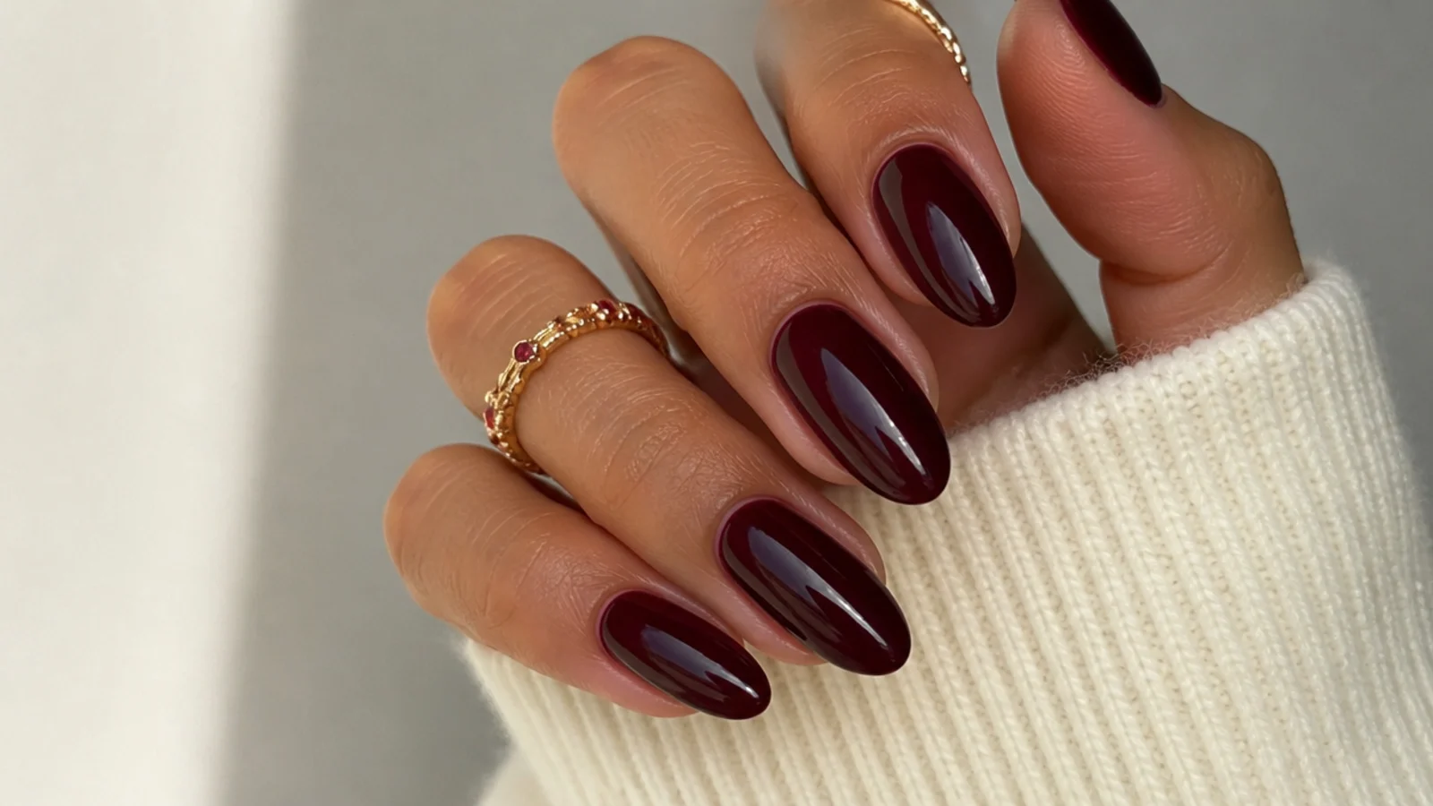 Glossy deep berry almond dark feminine aesthetic nails on a warm-toned hand
