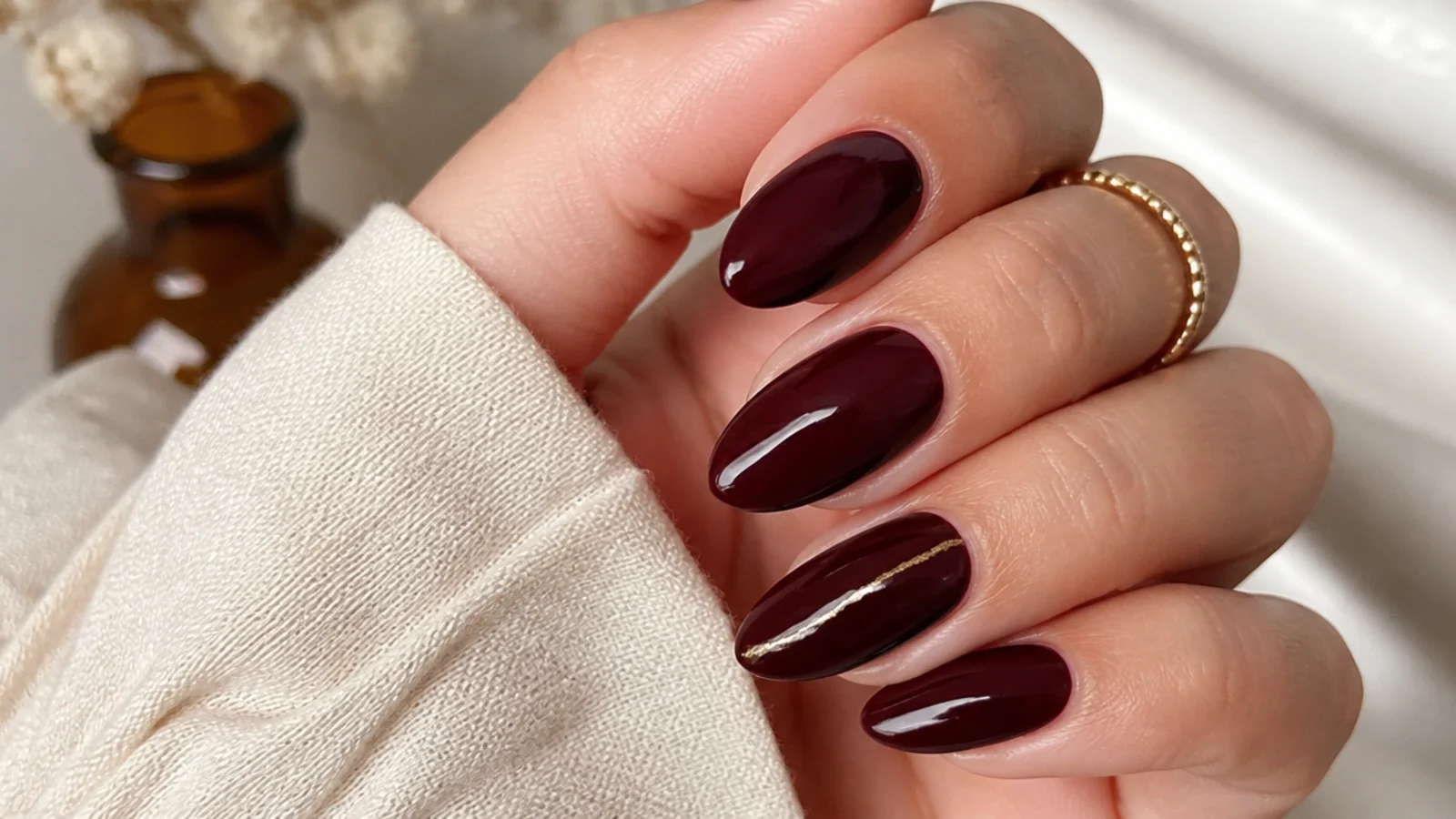 Glossy oxblood almond nails with a thin gold foil line on one accent nail