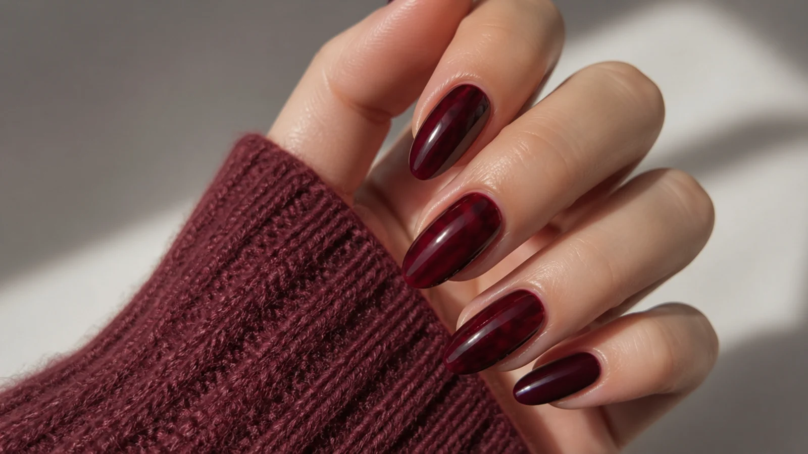 Glossy deep berry and oxblood almond nails showing warm dark feminine tones